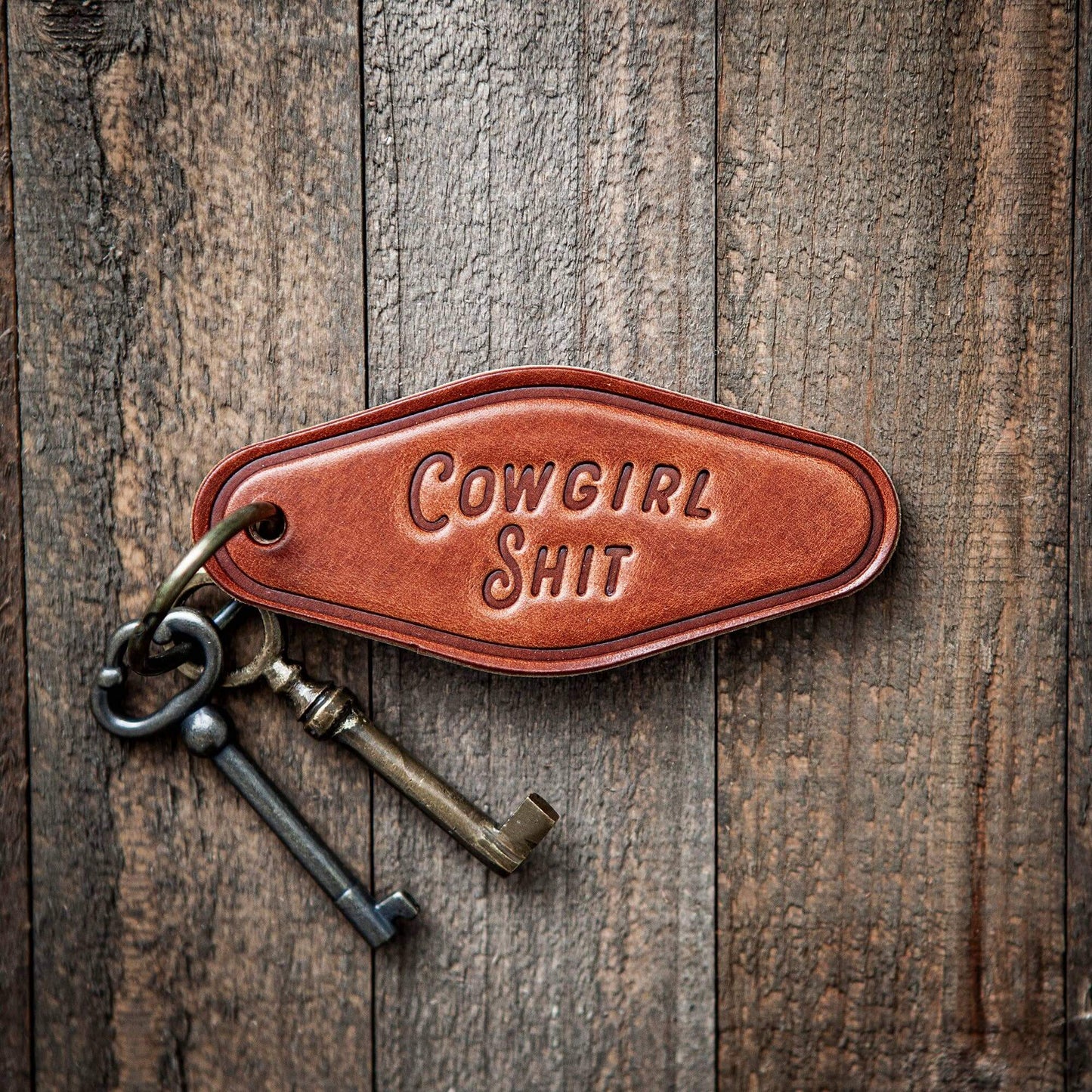 Cowgirl Shit Leather Keychain Motel Style featuring a bold stamp on rustic wood background.