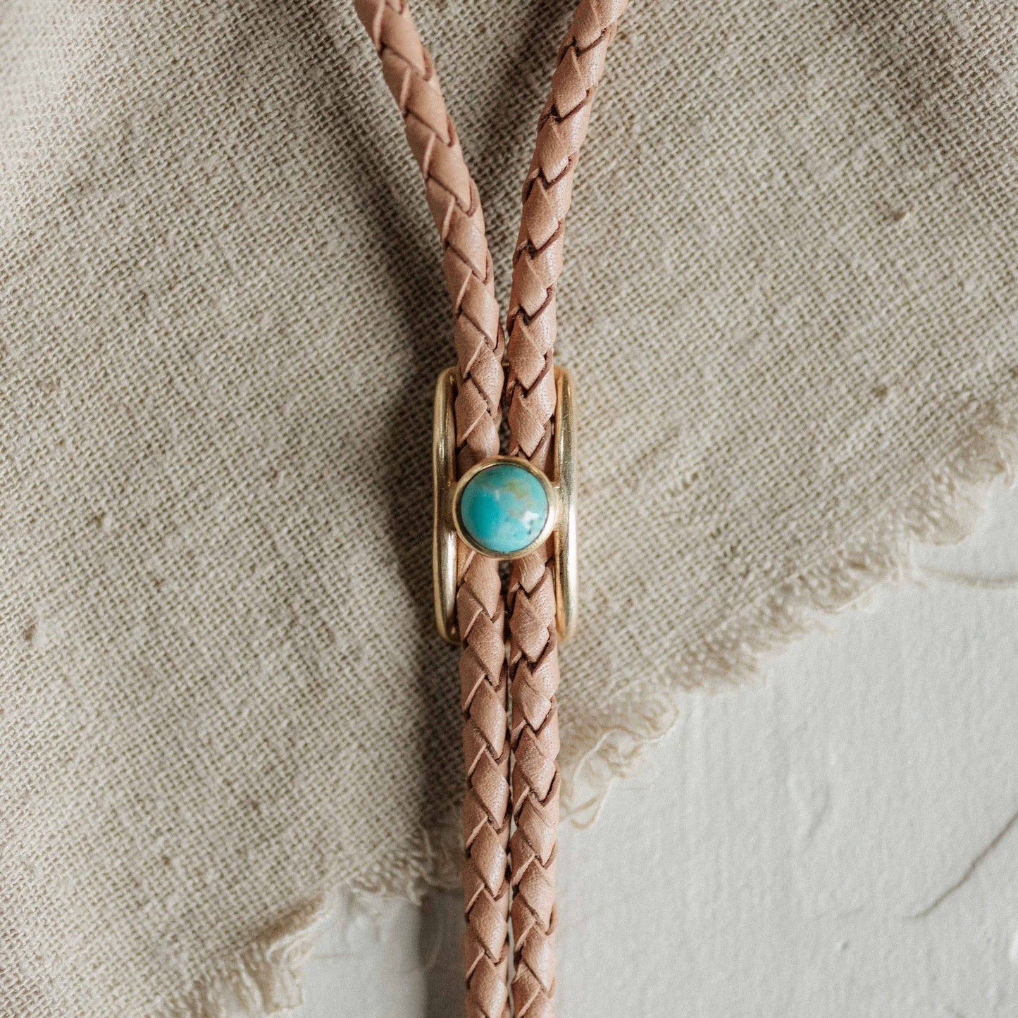 Leather bolo tie with turquoise stone on a textured beige background