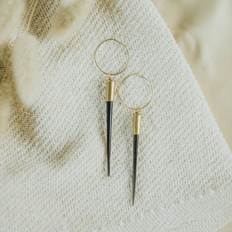 Gold hoop earrings with black accents on a textured beige fabric background