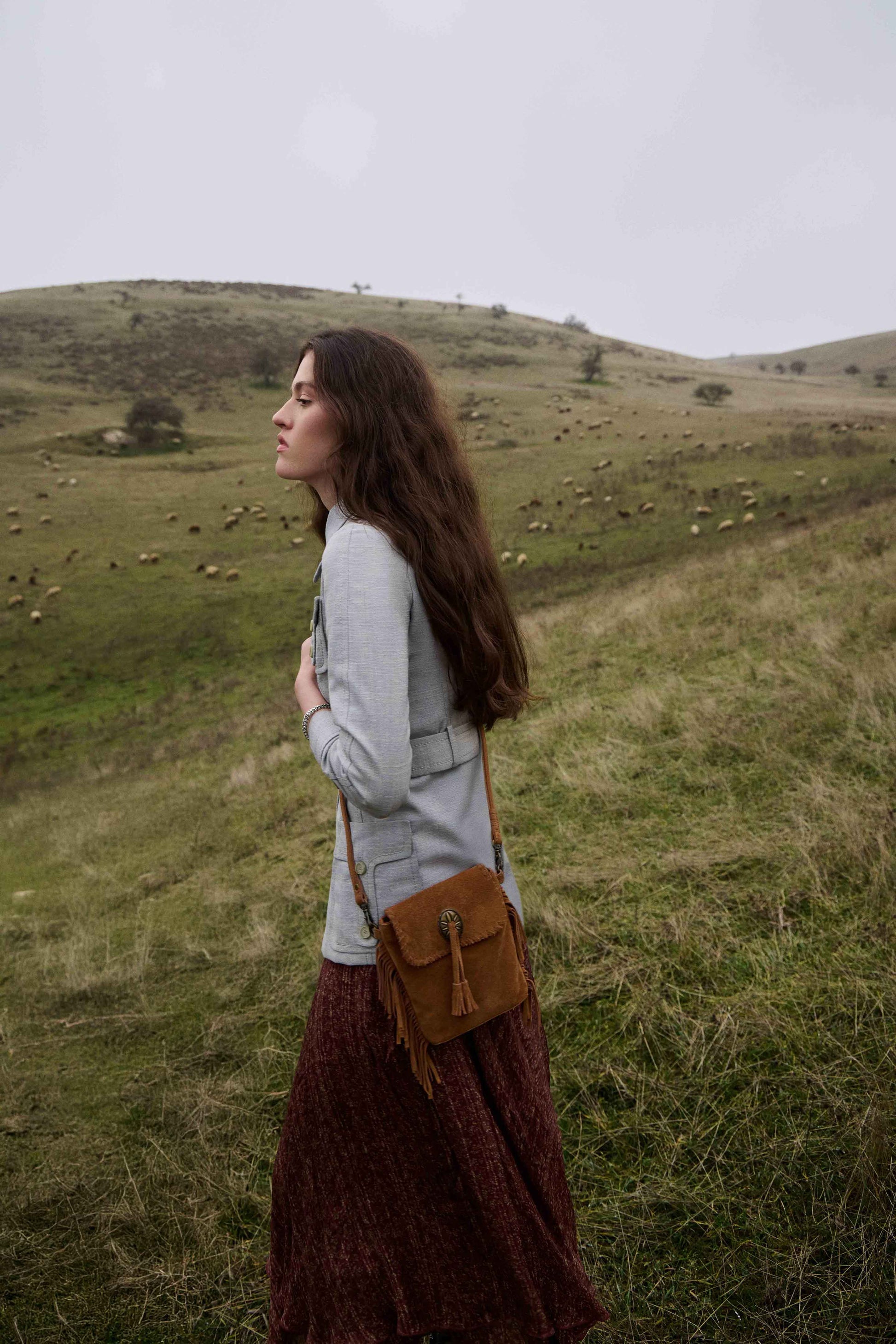 Woman standing in a field with sheep, holding a brown bag