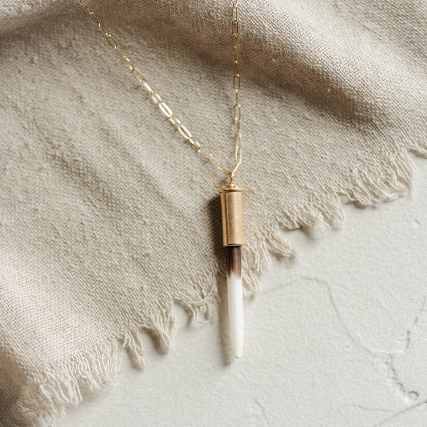 Necklace with a cylindrical pendant on a textured fabric background