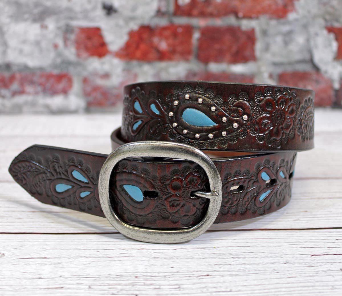 Genuine Leather belt with dark stained paisley floral embossing, turquoise painted sections edged with domed nail heads in silver finish, and removable oval buckle in silver finish. 1-1/2" wide with removable buckle. Imported