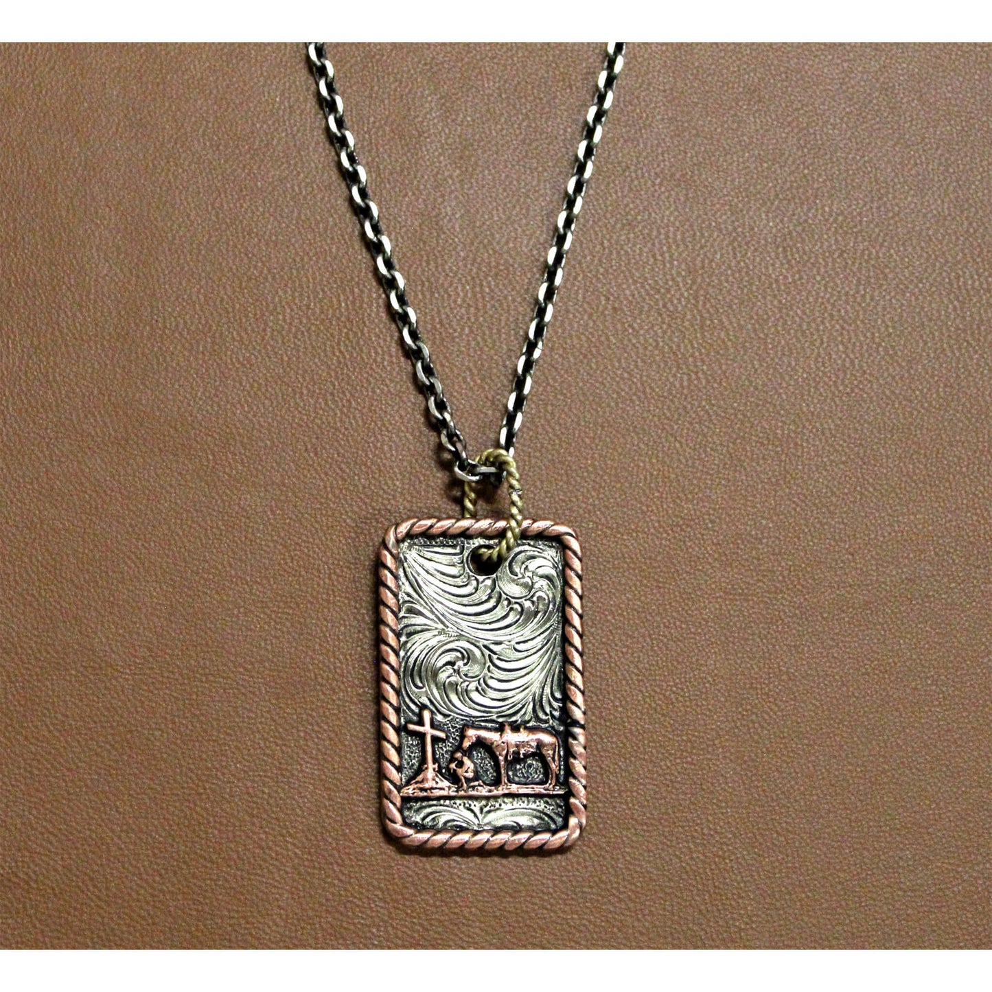 Beautiful antique silver dog tag style pendant with praying cowboy and floral scrolling. Rope edge in antique copper. Sterling Silver plated. 24 inch chain. Imported.