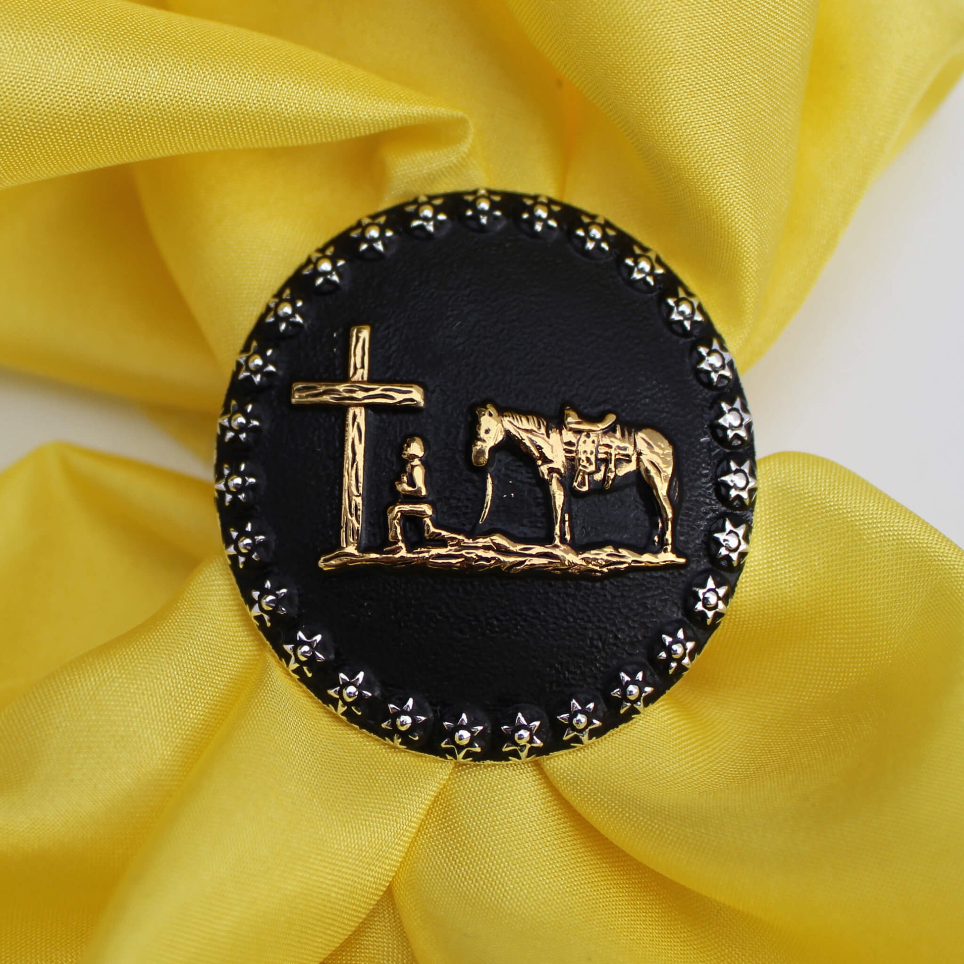 Secure your wild rag with a Cattle Kate Scarf Slide. This design features a praying cowboy on a black background with brass accents. An etched design borders the round slide measuring 1 1/2" diameter this slide is sure to last